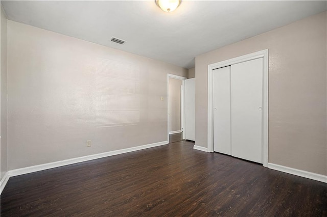 unfurnished bedroom featuring visible vents, baseboards, dark wood-type flooring, and a closet