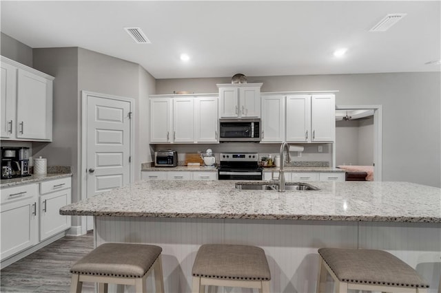 kitchen featuring stainless steel appliances, a kitchen island with sink, sink, and white cabinets