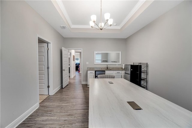 interior space featuring white cabinetry, a raised ceiling, hardwood / wood-style floors, and hanging light fixtures