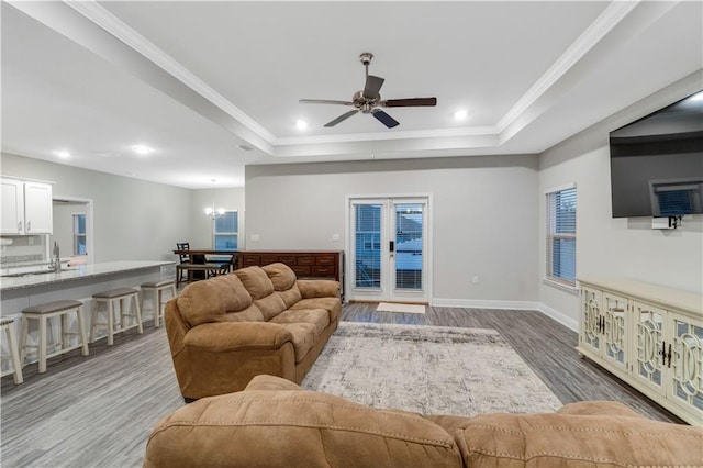 living room featuring crown molding, a tray ceiling, ceiling fan with notable chandelier, and light hardwood / wood-style floors