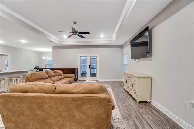 living room featuring crown molding, wood-type flooring, a tray ceiling, and ceiling fan with notable chandelier