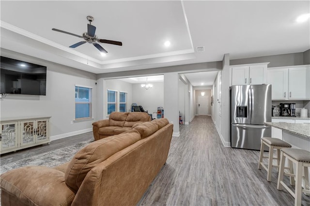 living room featuring a tray ceiling, ceiling fan with notable chandelier, and light hardwood / wood-style floors