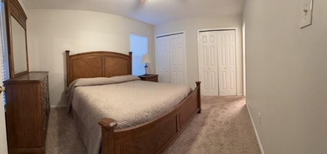 bedroom with baseboards, two closets, and light colored carpet