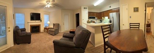 living room featuring light carpet, a fireplace, and ceiling fan