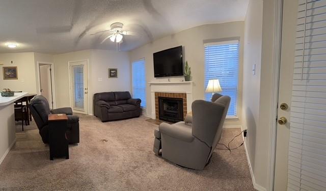 living area featuring carpet, a fireplace, baseboards, and a ceiling fan