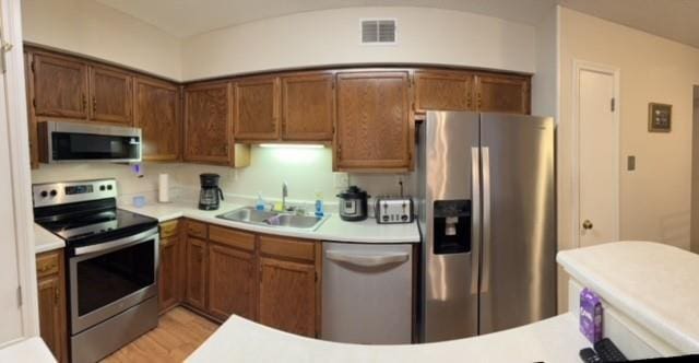 kitchen featuring stainless steel appliances, light countertops, visible vents, brown cabinetry, and a sink