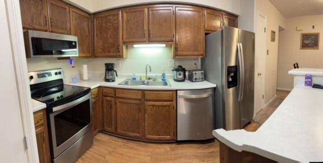 kitchen with light countertops, appliances with stainless steel finishes, brown cabinetry, and a sink