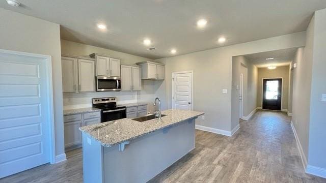 10706 Relic Rd N, Mobile, AL 36608 - kitchen with appliances with stainless steel finishes, a kitchen island with sink, light wood-style flooring, recessed lighting, and light stone countertops