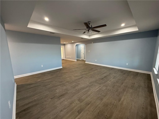 empty room with a tray ceiling, ceiling fan, and dark wood-type flooring