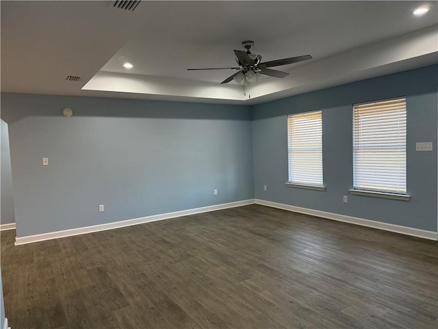 empty room with ceiling fan, dark wood-type flooring, and a tray ceiling