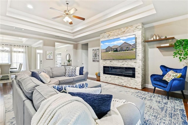 living room featuring hardwood / wood-style floors, a stone fireplace, a raised ceiling, crown molding, and ceiling fan