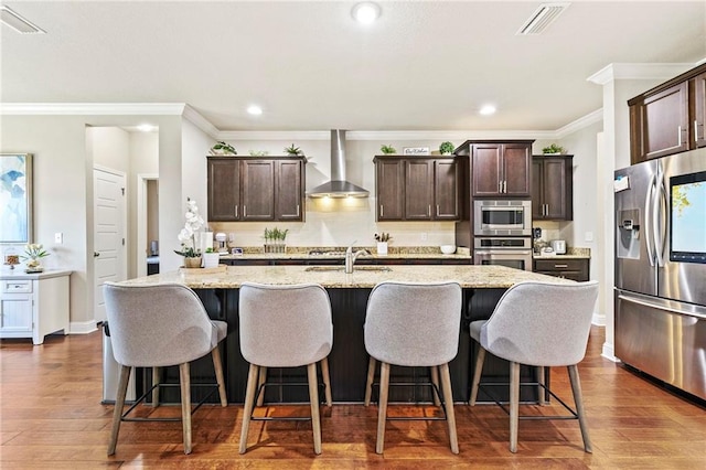 kitchen featuring stainless steel appliances, dark hardwood / wood-style floors, wall chimney exhaust hood, and an island with sink