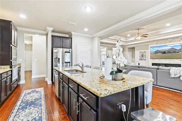 kitchen with light stone countertops, dark hardwood / wood-style flooring, crown molding, sink, and an island with sink