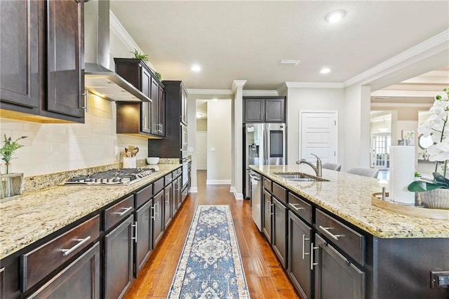 kitchen featuring appliances with stainless steel finishes, light wood-type flooring, ornamental molding, sink, and wall chimney range hood