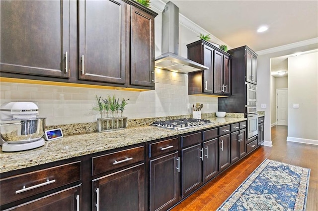 kitchen featuring dark brown cabinetry, wall chimney exhaust hood, dark wood-type flooring, decorative backsplash, and appliances with stainless steel finishes