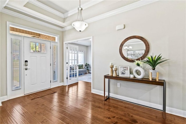 foyer featuring a notable chandelier, ornamental molding, dark wood-type flooring, and a tray ceiling