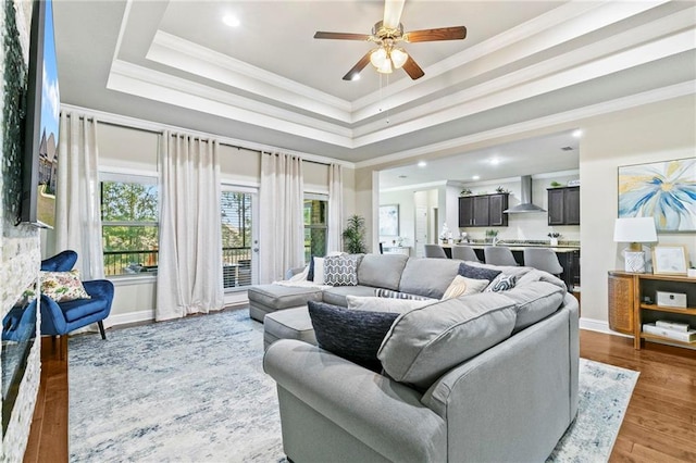 living room featuring a tray ceiling, ceiling fan, ornamental molding, and hardwood / wood-style flooring