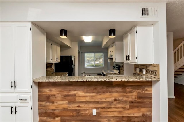 kitchen with light stone counters, white range with electric stovetop, black fridge, backsplash, and wood-type flooring