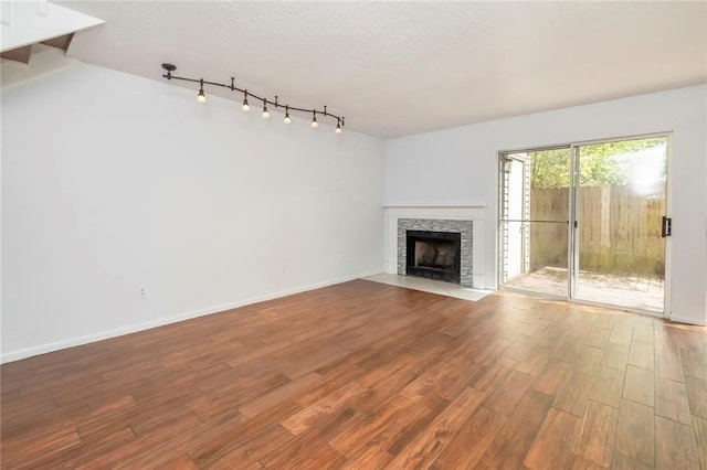 unfurnished living room featuring rail lighting, a stone fireplace, and light wood-type flooring