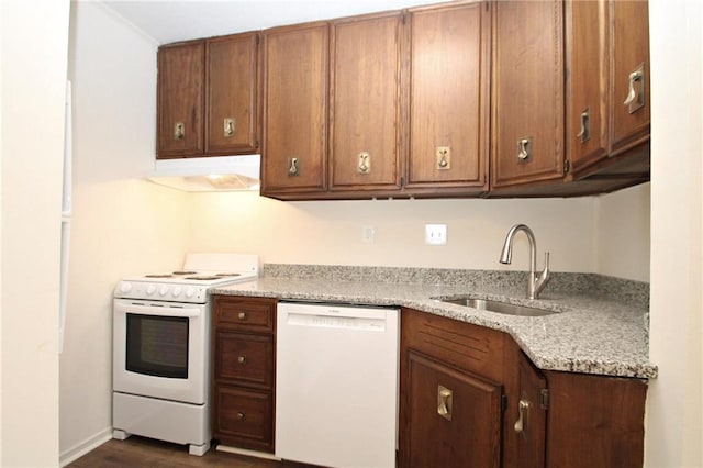 kitchen with white appliances, under cabinet range hood, brown cabinets, and a sink