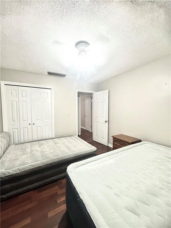 bedroom featuring ceiling fan, a textured ceiling, dark hardwood / wood-style flooring, and a closet