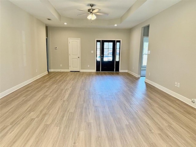 unfurnished room featuring a tray ceiling, wood finished floors, baseboards, and ceiling fan