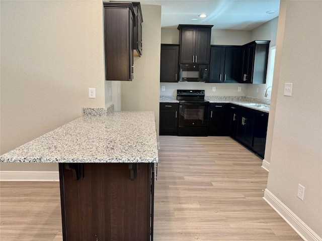 kitchen featuring a sink, a peninsula, black appliances, light wood-type flooring, and baseboards
