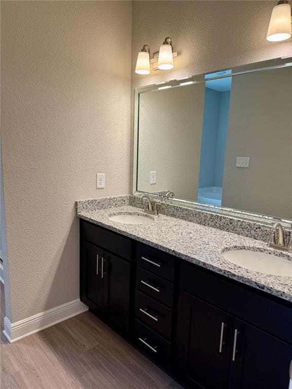 full bath with double vanity, a textured wall, wood finished floors, and a sink
