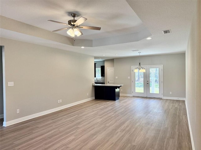 unfurnished living room featuring light wood-style flooring, a tray ceiling, visible vents, baseboards, and ceiling fan