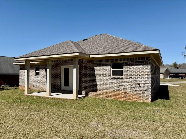 rear view of house with a yard, a shingled roof, brick siding, and a patio