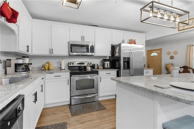 kitchen featuring white cabinetry, stainless steel appliances, sink, hanging light fixtures, and light hardwood / wood-style floors