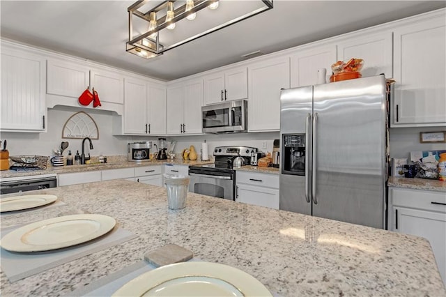 kitchen with light stone counters, sink, appliances with stainless steel finishes, and white cabinetry