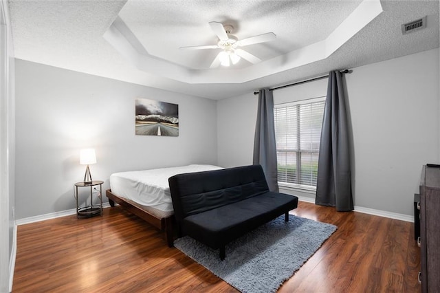 bedroom featuring a tray ceiling, ceiling fan, a textured ceiling, and dark hardwood / wood-style floors