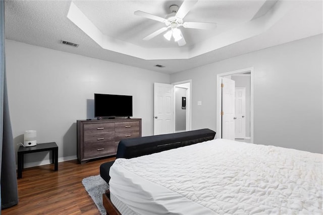 bedroom with a raised ceiling, ceiling fan, dark wood-type flooring, and a textured ceiling