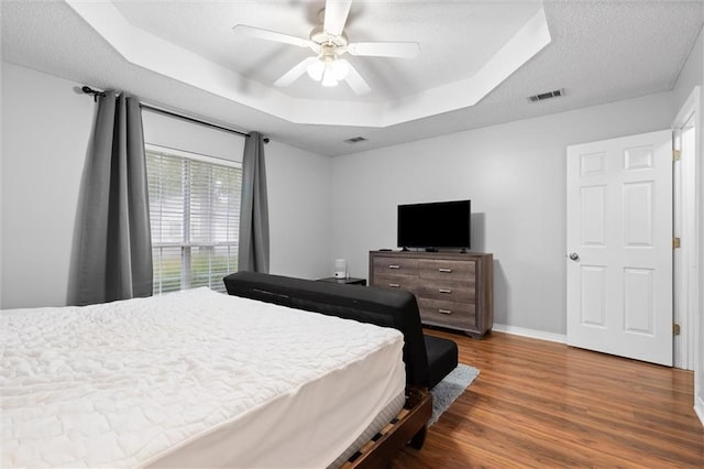 bedroom with a raised ceiling, ceiling fan, a textured ceiling, and dark hardwood / wood-style floors