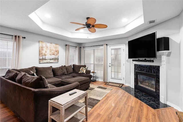 living room featuring dark hardwood / wood-style flooring, a raised ceiling, a healthy amount of sunlight, and a premium fireplace