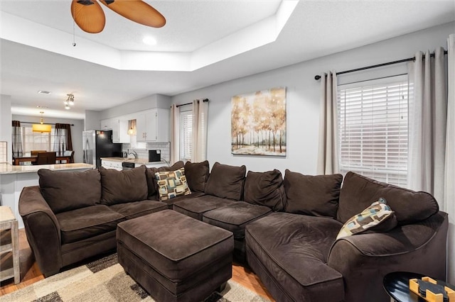 living room featuring light hardwood / wood-style floors, ceiling fan, and a tray ceiling