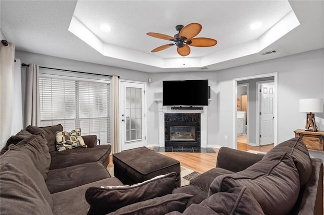 living room with ceiling fan, wood-type flooring, a fireplace, and a tray ceiling