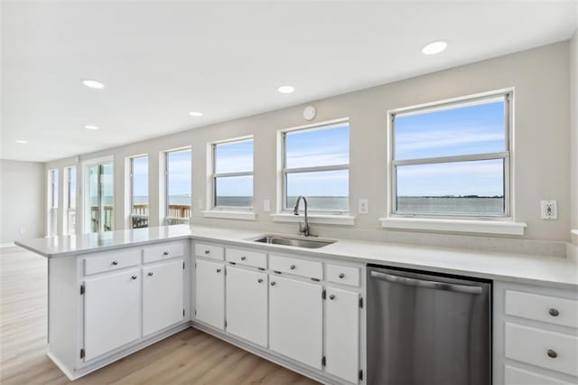 kitchen with sink, stainless steel dishwasher, kitchen peninsula, plenty of natural light, and white cabinets