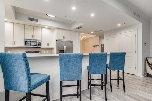 kitchen featuring tasteful backsplash, light hardwood / wood-style floors, stainless steel appliances, white cabinets, and a breakfast bar area