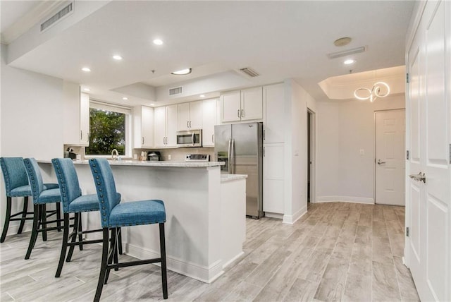 kitchen featuring kitchen peninsula, white cabinets, a breakfast bar area, appliances with stainless steel finishes, and light hardwood / wood-style flooring