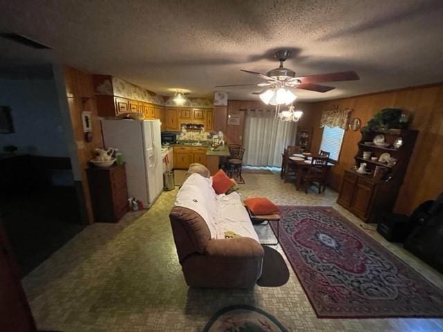 living room with ceiling fan, wood walls, light carpet, and a textured ceiling