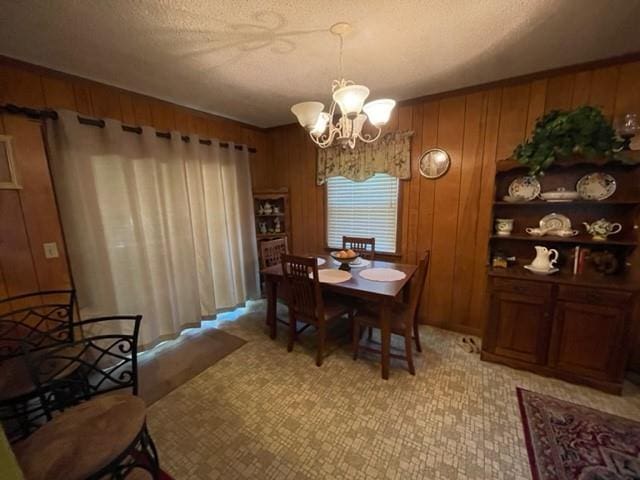 dining area featuring a chandelier, a textured ceiling, and wooden walls