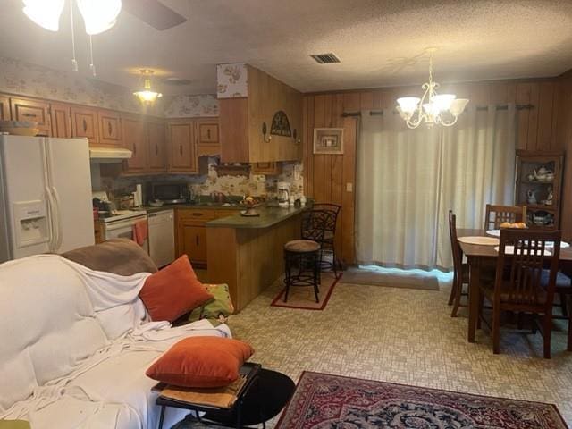 kitchen with wooden walls, ceiling fan with notable chandelier, pendant lighting, and white appliances