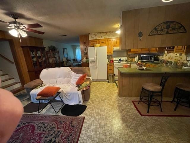 kitchen featuring a kitchen bar, kitchen peninsula, ceiling fan, and white appliances