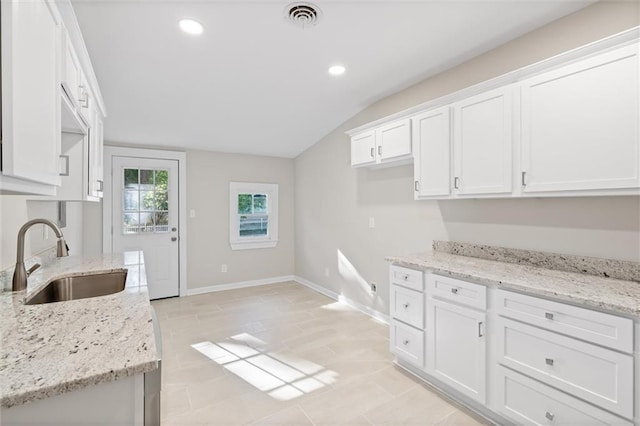 kitchen featuring lofted ceiling, white cabinets, light tile patterned floors, light stone countertops, and sink