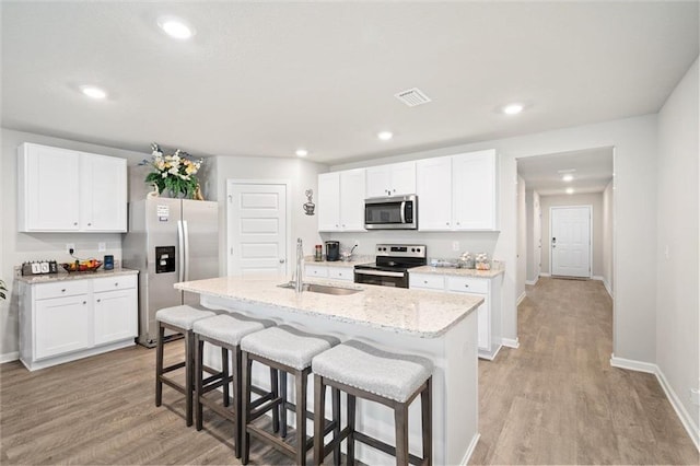 kitchen with a kitchen island with sink, white cabinets, sink, light hardwood / wood-style floors, and stainless steel appliances