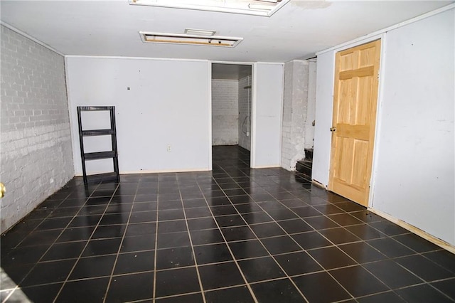 unfurnished room with brick wall and dark tile patterned flooring