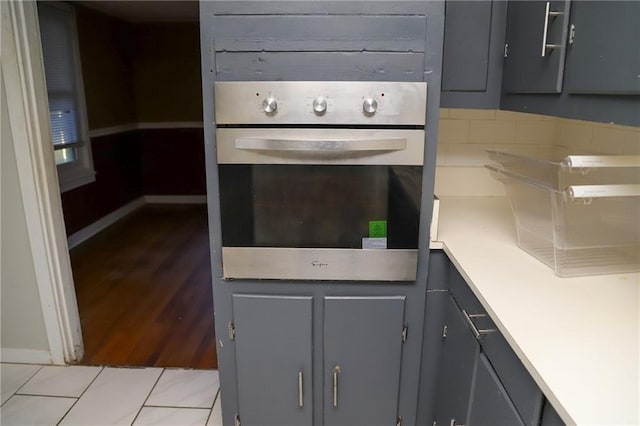 kitchen featuring light tile patterned floors, light countertops, gray cabinetry, stainless steel oven, and baseboards