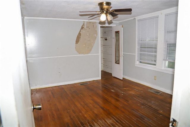 spare room featuring dark wood-type flooring, a ceiling fan, visible vents, and baseboards